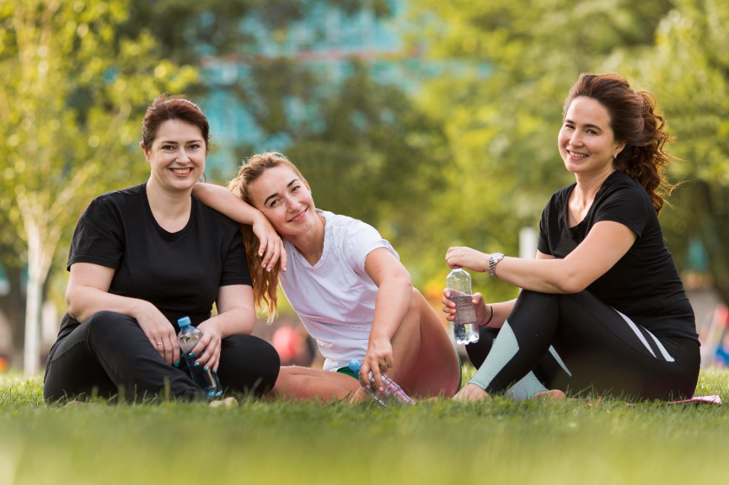 Tres mujeres descansando en un parque después de hacer ejercicio, representando bienestar y comunidad